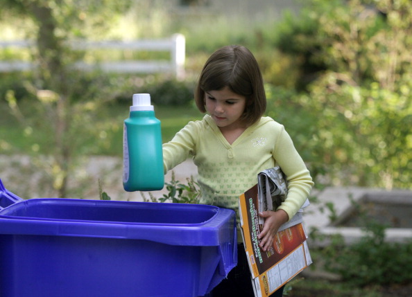 Young child placing recyclable items into large blue recycle bin (Photo by: Digital Light Source/UIG via Getty Images)